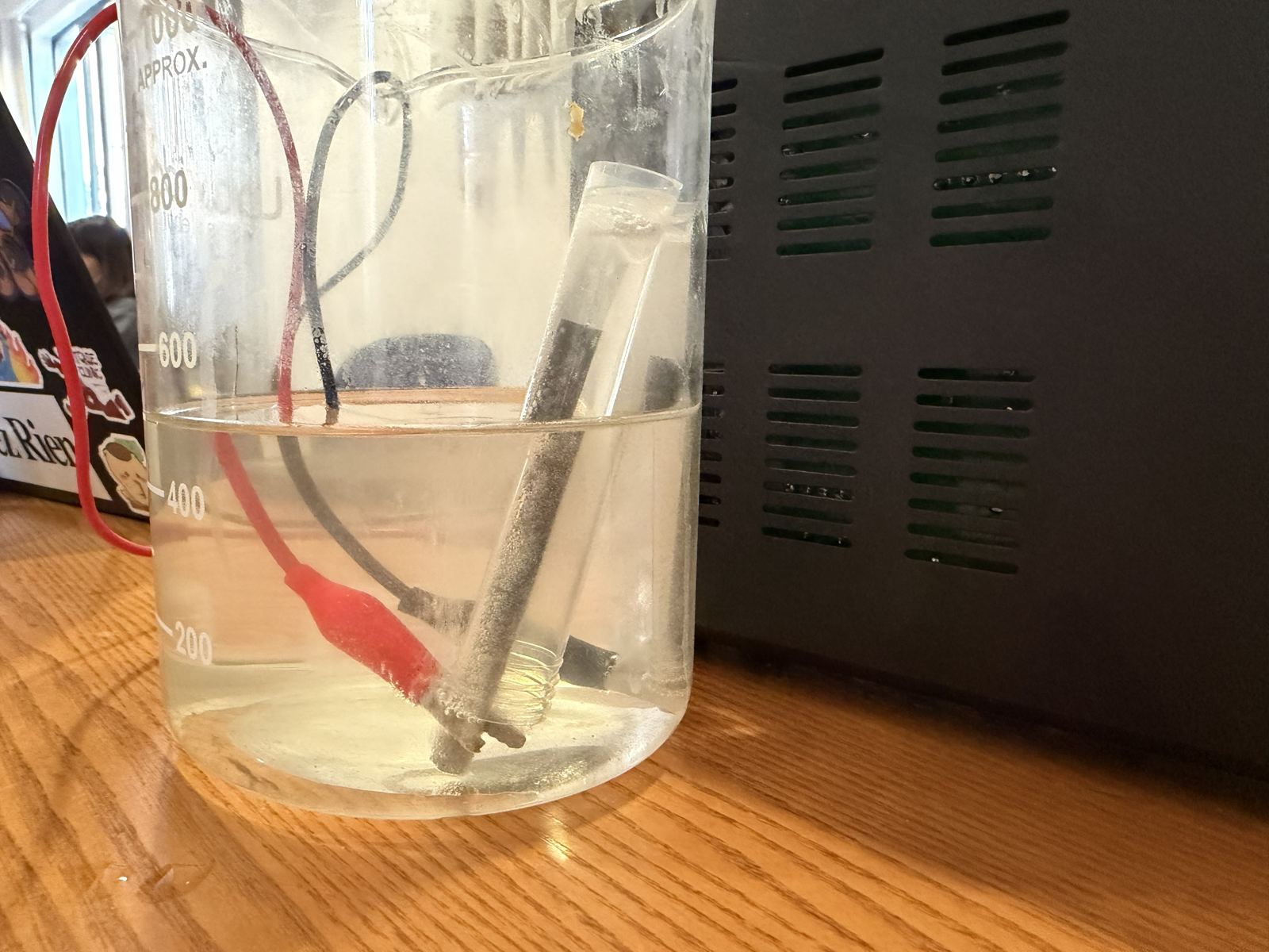 Close-up of a graphite electrode inside a gas collection tube in the electrolyte, with small bubbles on the electrode surface.